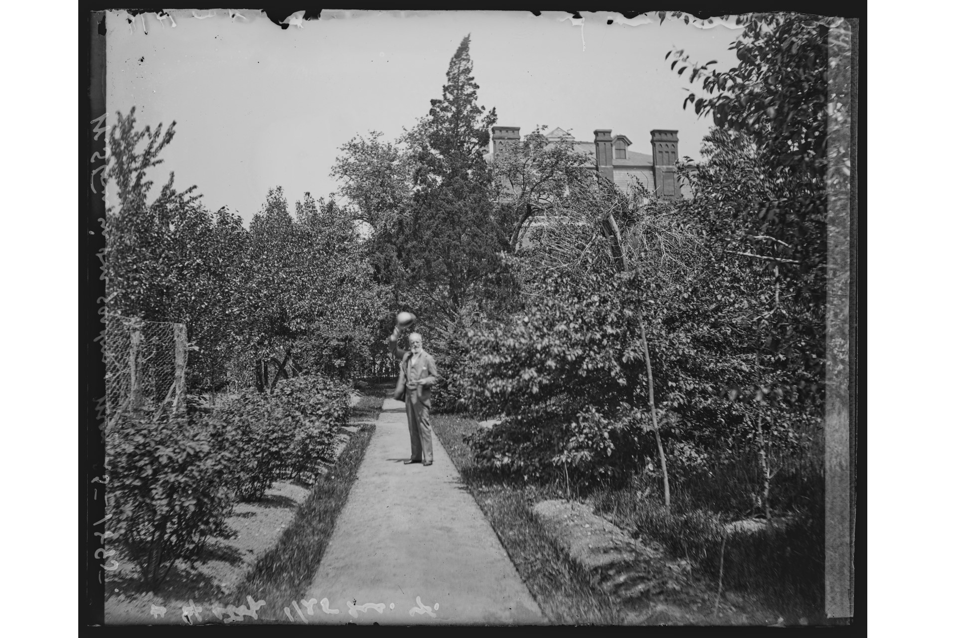 black and white photo of man in garden lifting hat