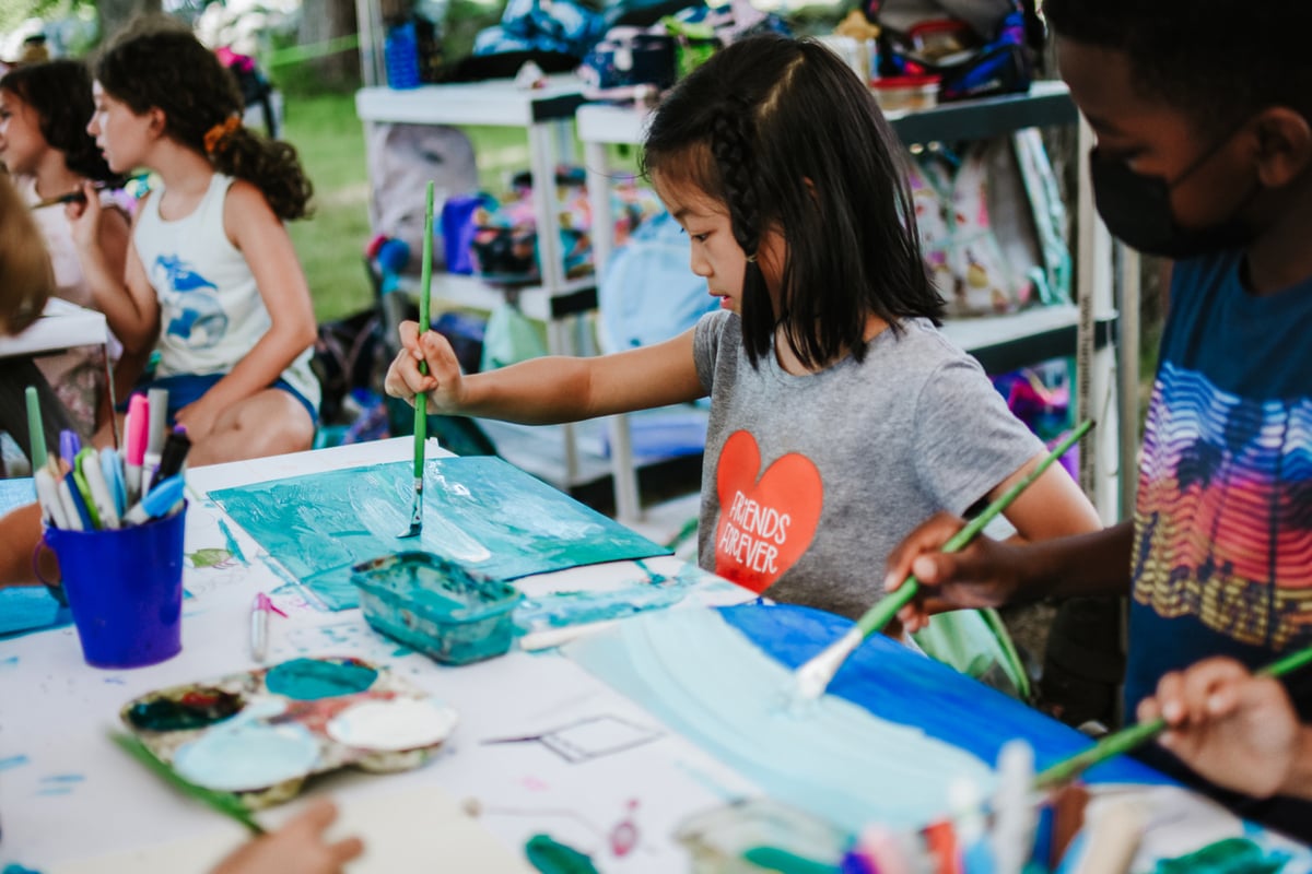 Young camper painting at a table outdoors