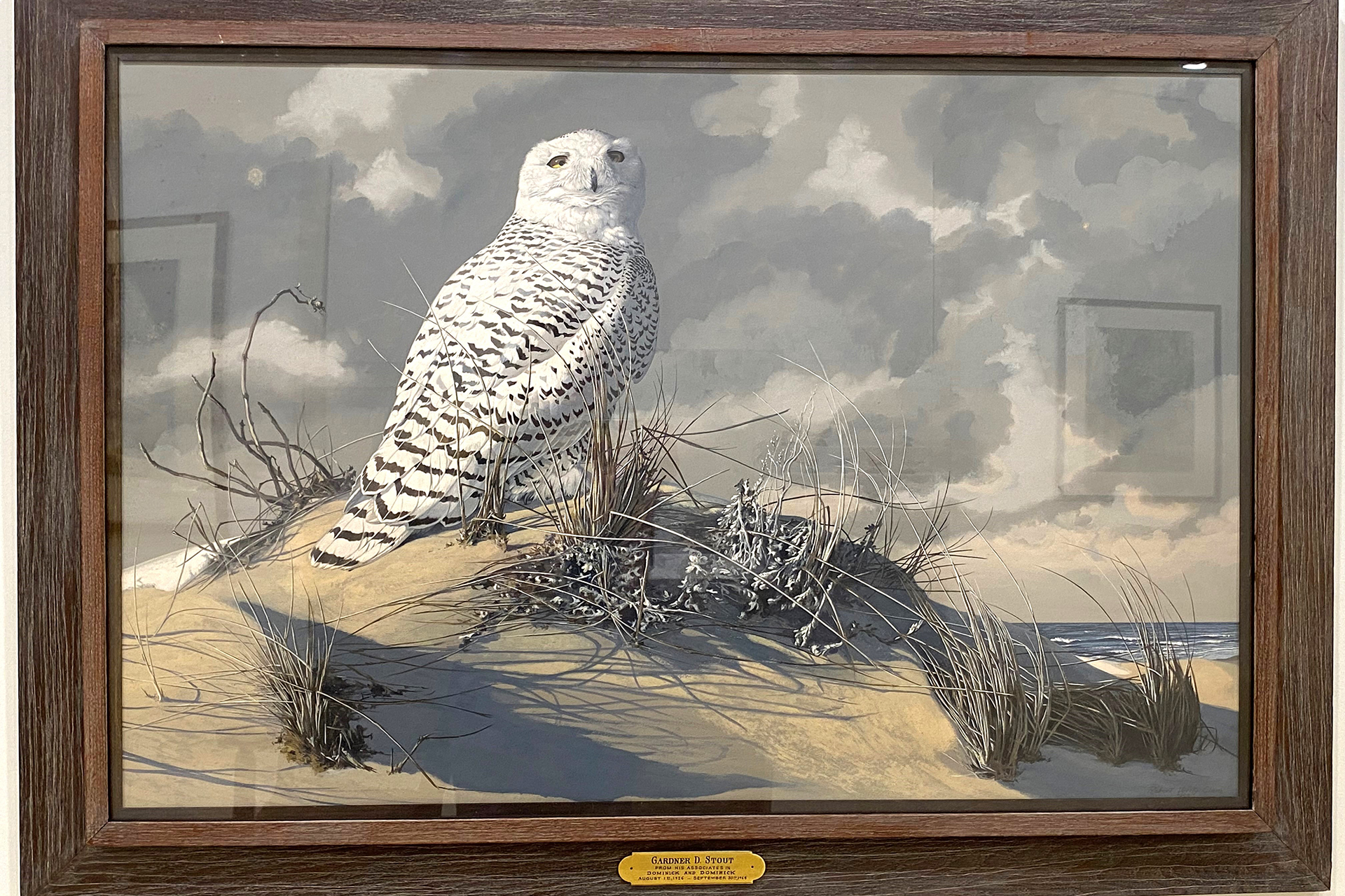 Gouache painting of a snowy owl perched on a sand dune against gray, pillowy clouds