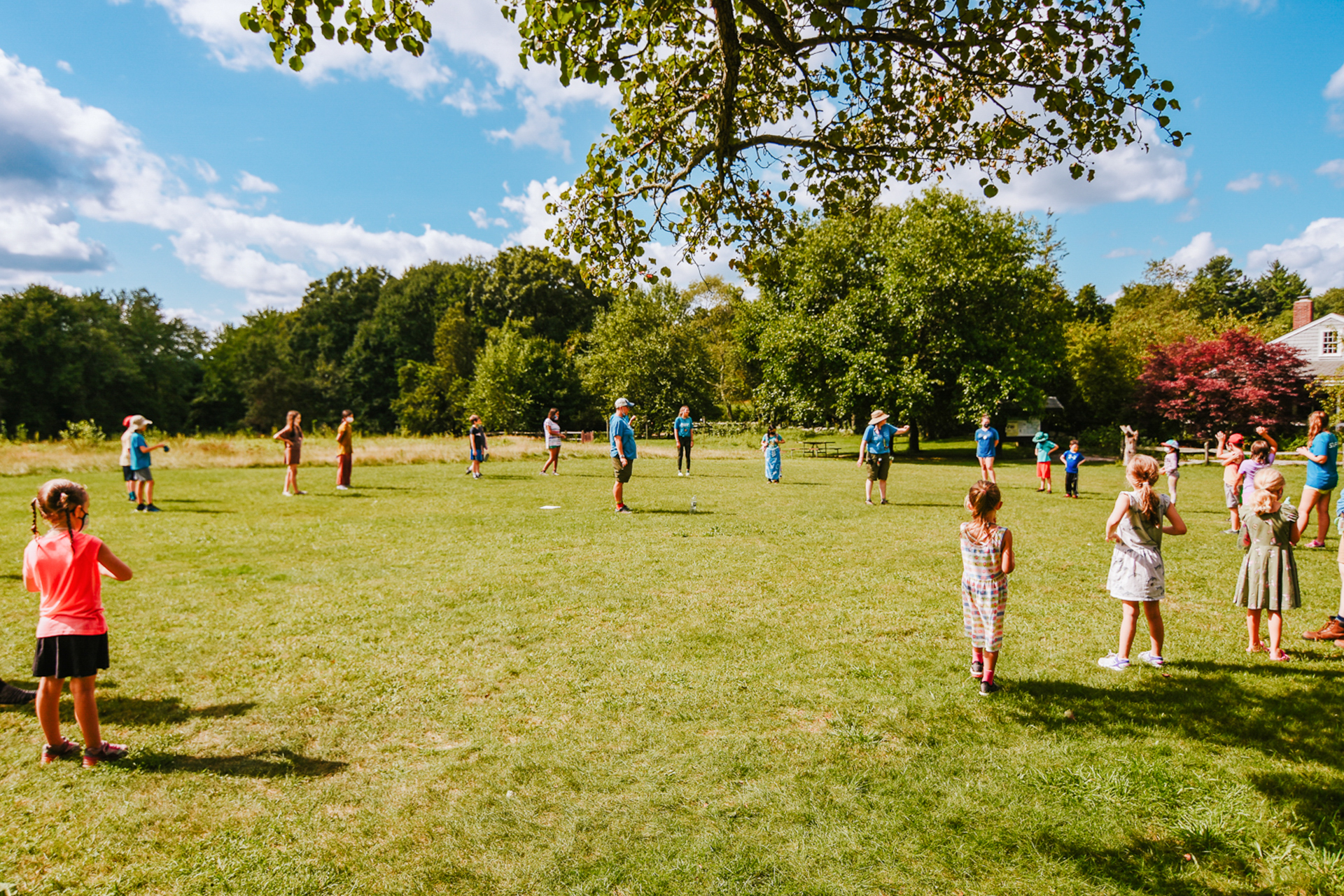 Campers at Stony Brook Nature Camp gather in a large circle on the activity field, listening to the camp directors in the middle explaining the next game