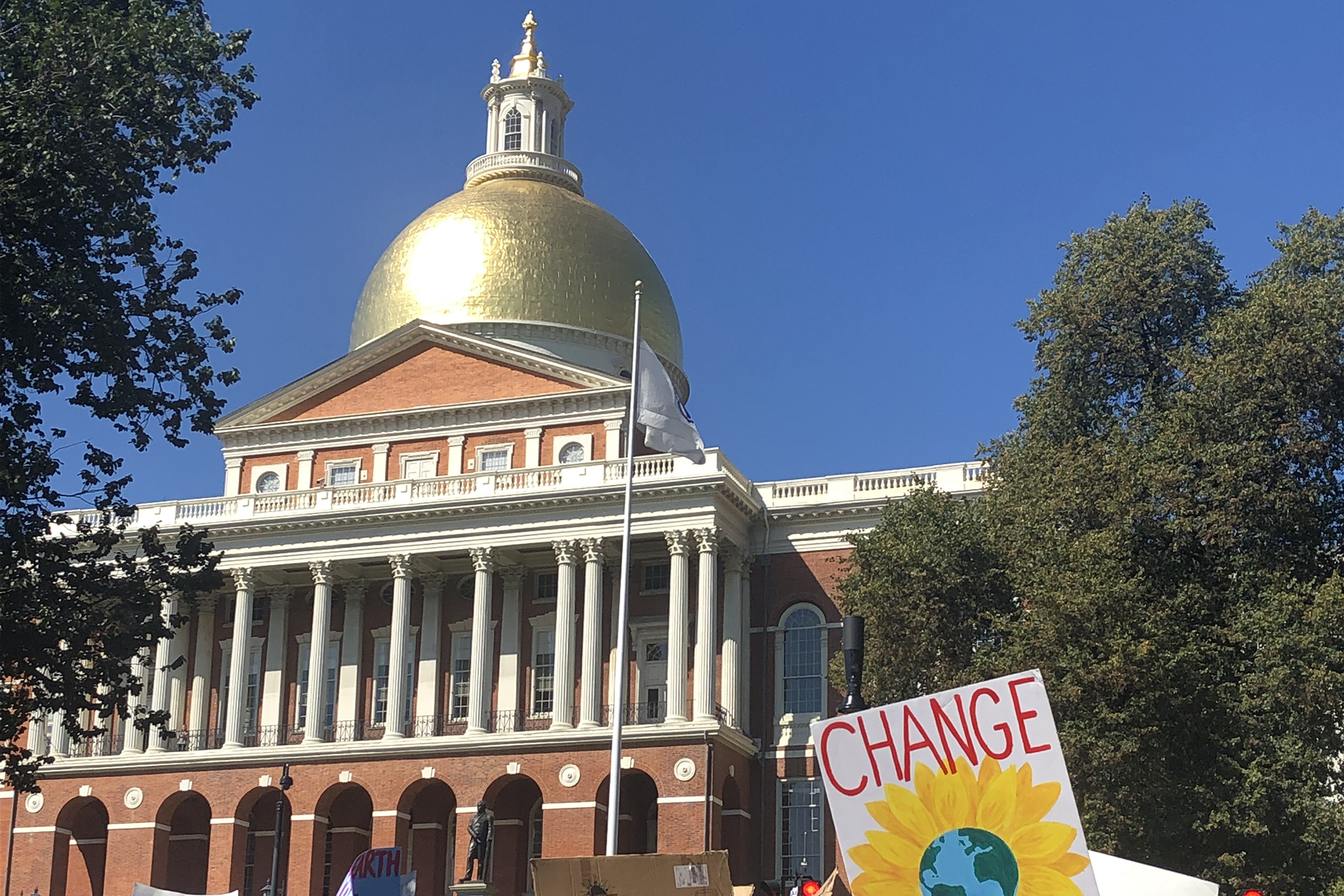 A sign reading "Change" held up in front of the Massachusetts State House