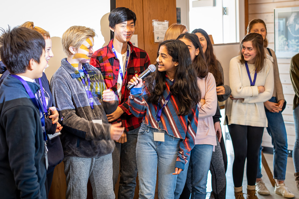 Teen speaking into a microphone surrounded by other teens