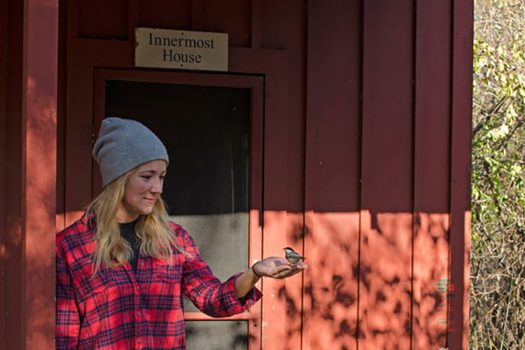 Woman standing in front of red cabin holding a chickadee