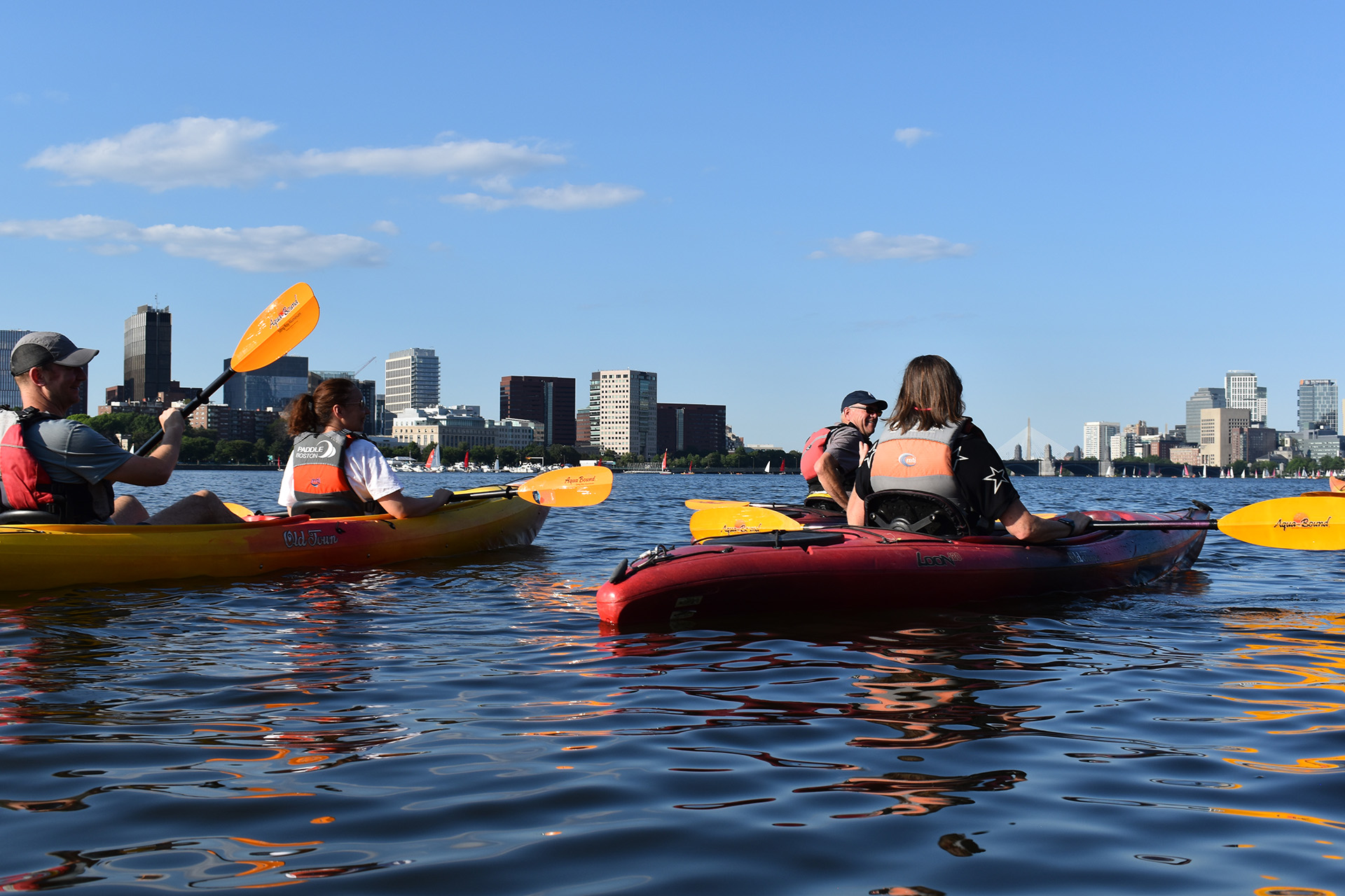Four people kayaking with Boston's skyline in the background
