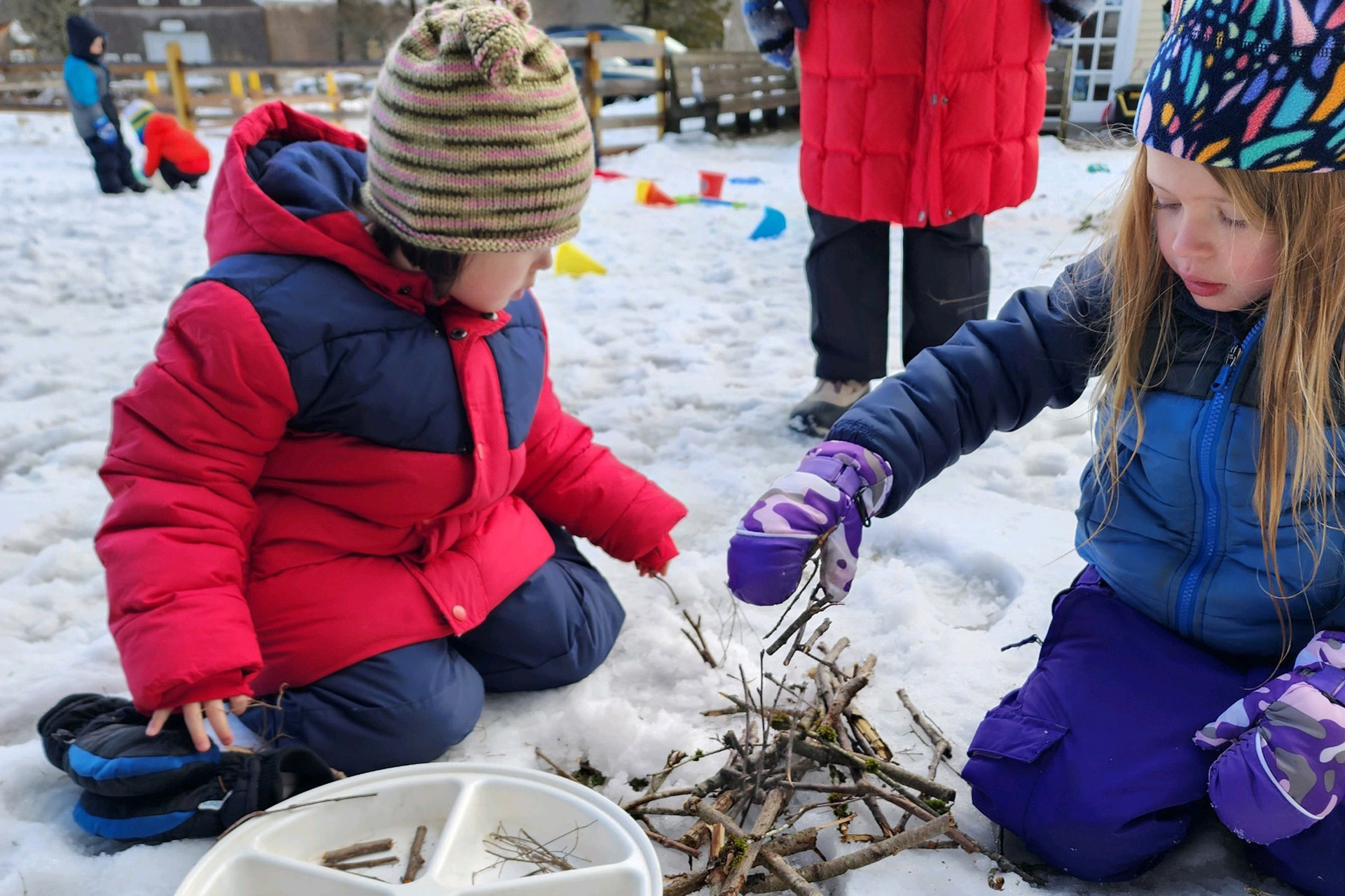 two preschoolers creating a sculpture of twigs in the snow