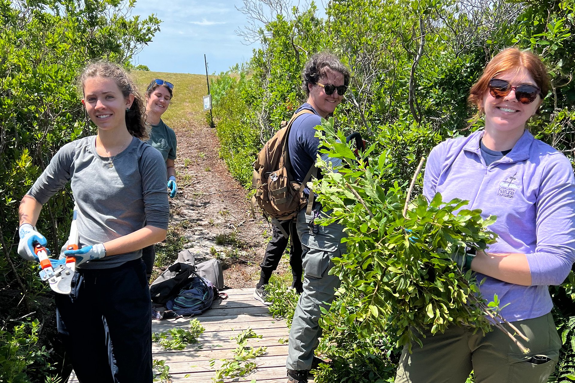 YES Stewards helping to prune plants growing along a trail