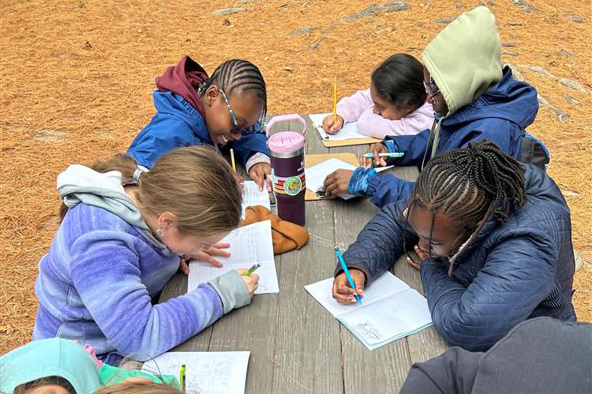 Students filling out workbooks at a picnic table