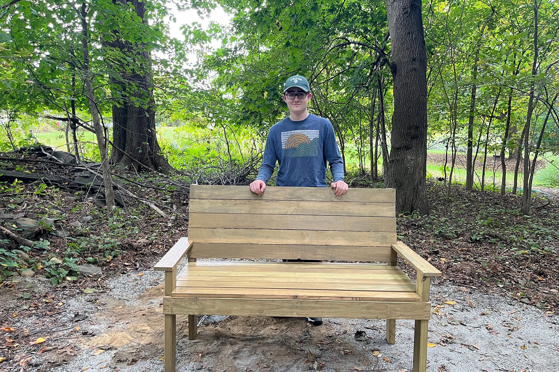 Oliver Chase-Norris posing behind BMB's new bench on the All Persons Trail